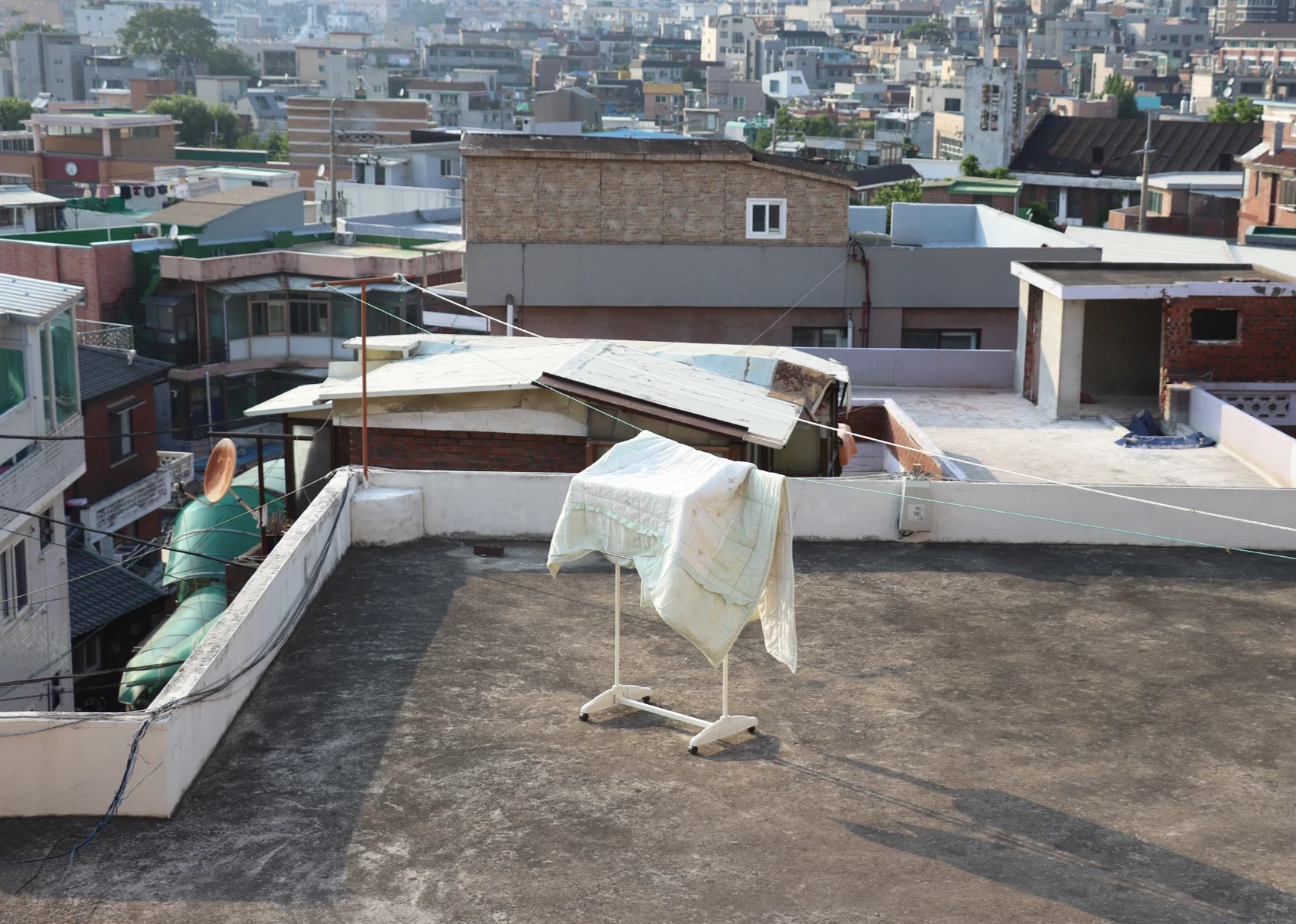 A quilt drying on a rack on a concrete rooftop, the city stretching behind