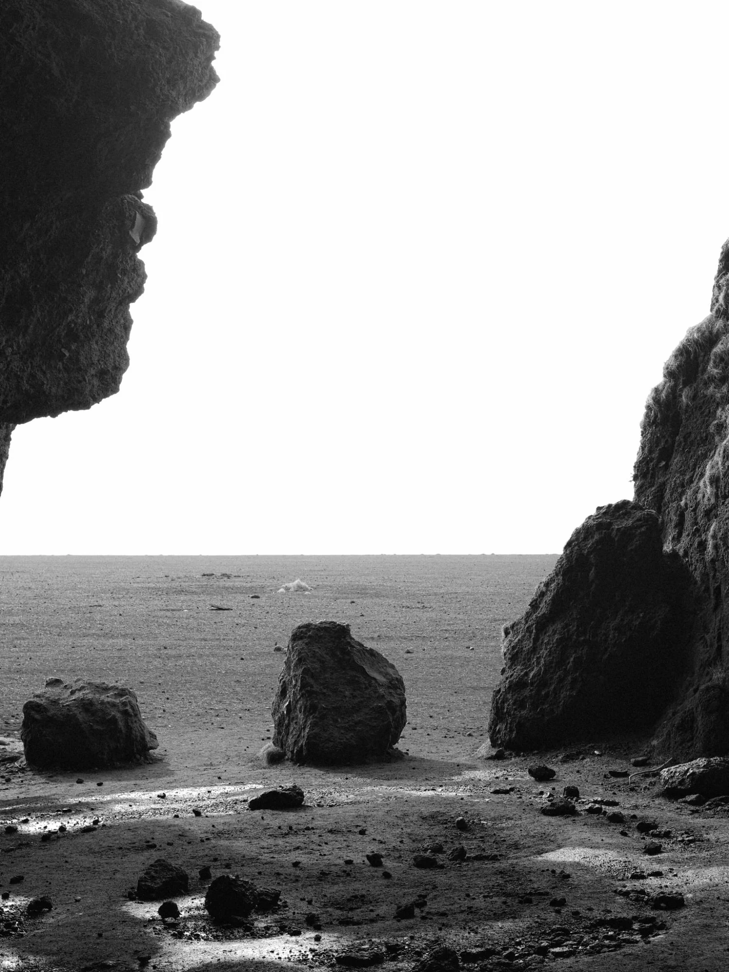 Black and white: boulders on the floor of an empty sea cave, the open shore beyond